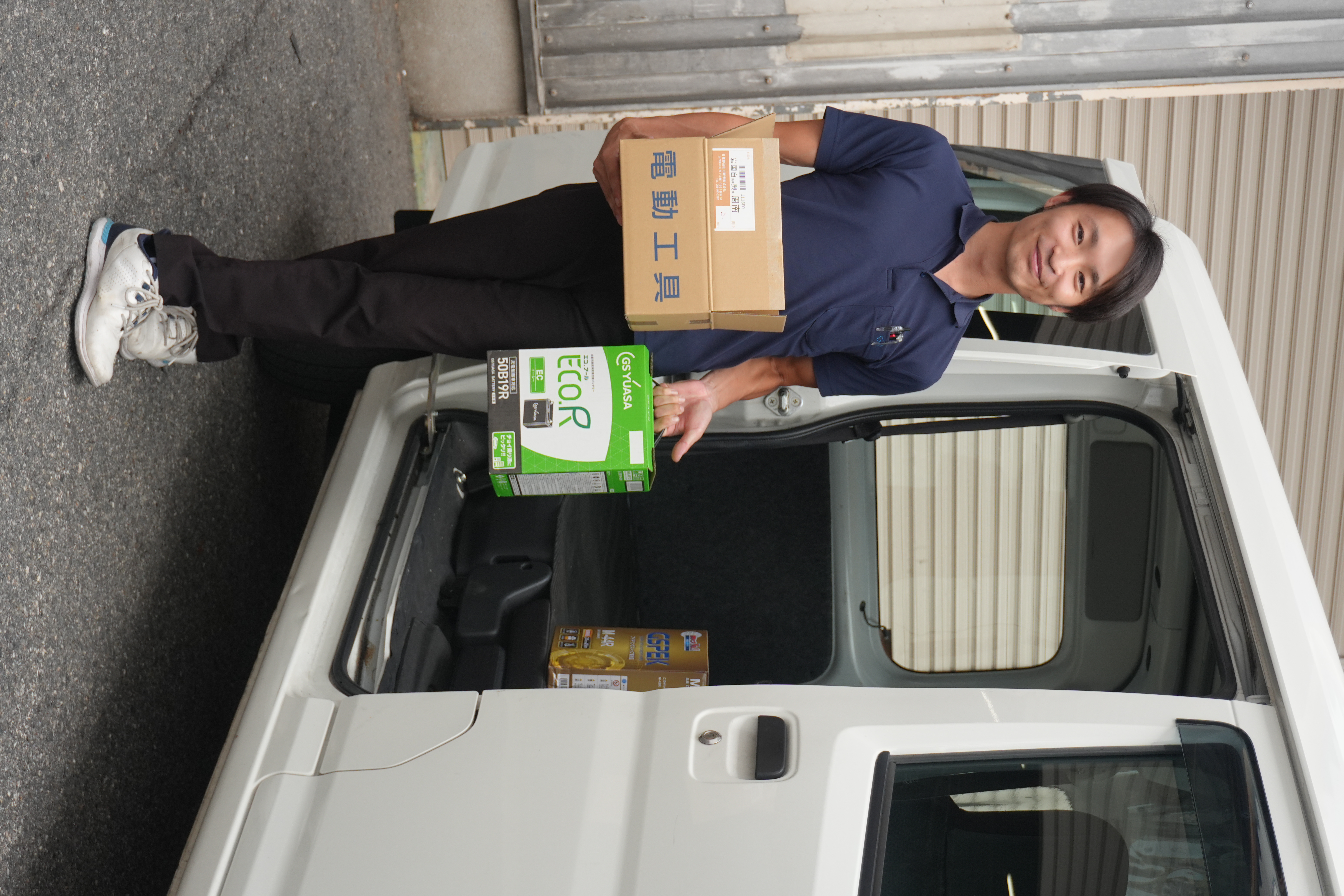 社用車の前で部品を持つ社員